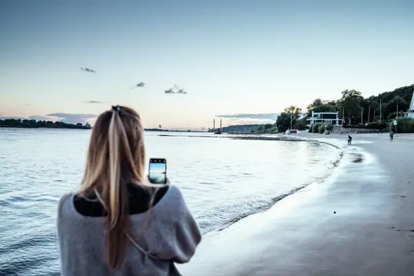 Eine blonde Frau fotografiert den Strand Richtung Wittenbergen und die Elbe bei Sonnenuntergang.