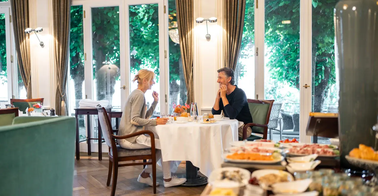 Ein Mann und eine Frau in festlicher Kleidung stehen auf einem Balkon vor einem See.