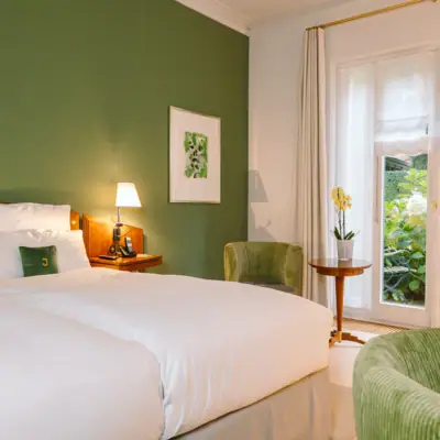 Zimmer mit Hotel Louis C. Jacob mit einem Bett vor einer grünen Wand, sowie zwei grünen Sesseln und einem Beistelltisch.
