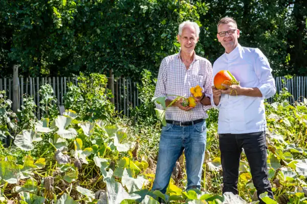 Thomas Martin und ein Mitarbeiter des Botanischen Gartens stehen in einem Garten und halten geerntete Kürbisse.