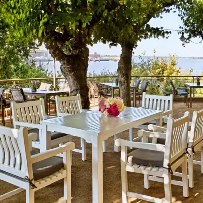 Weiße Tischgruppe unter Bäumen auf der Lindenterrasse.