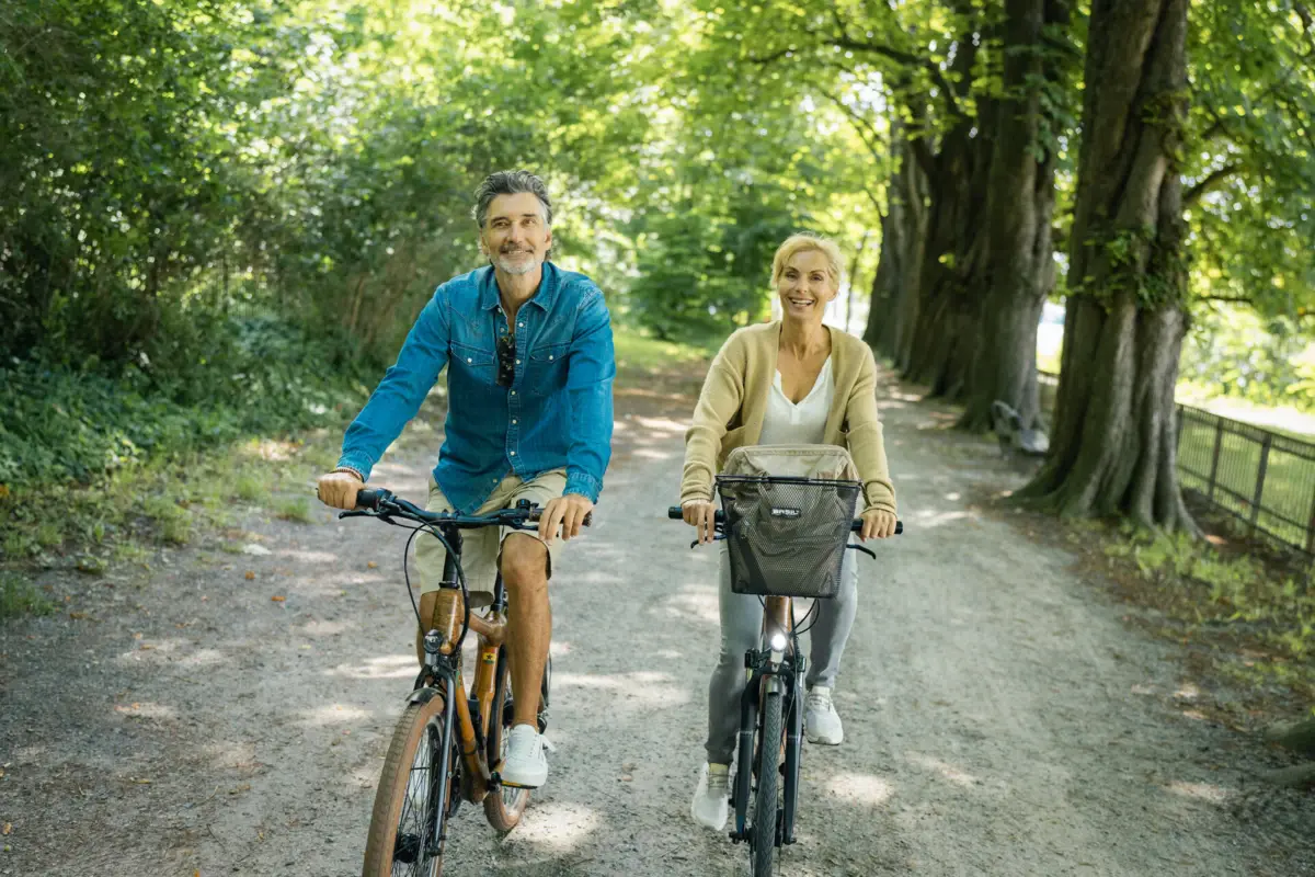 Ein Mann und eine Frau fahren Fahrrad auf einem Fahrradweg gesäumt von Bäumen und Hecken entlang der Elbe.