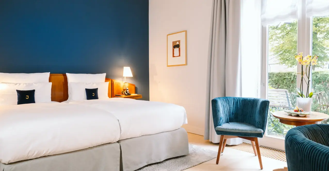 Interior view of a hotel room with a bed and a chair at the Louis C. Jacob in Hamburg.