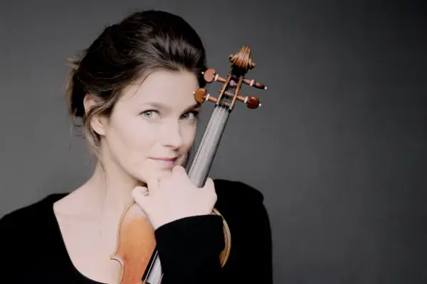 Janine Jansen steht vor einem grauen Hintergrund und hält eine Geige im Arm.