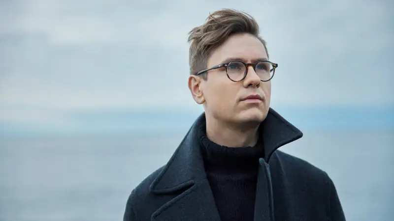 Víkingur Ólafsson trägt einen schwarzen Pullover und einen schwarzen Mantel und schaut in die Ferne.