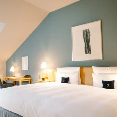 Bett vor einer hellblauen Wand mit Gemälde im Hotel Louis C. Jacob.