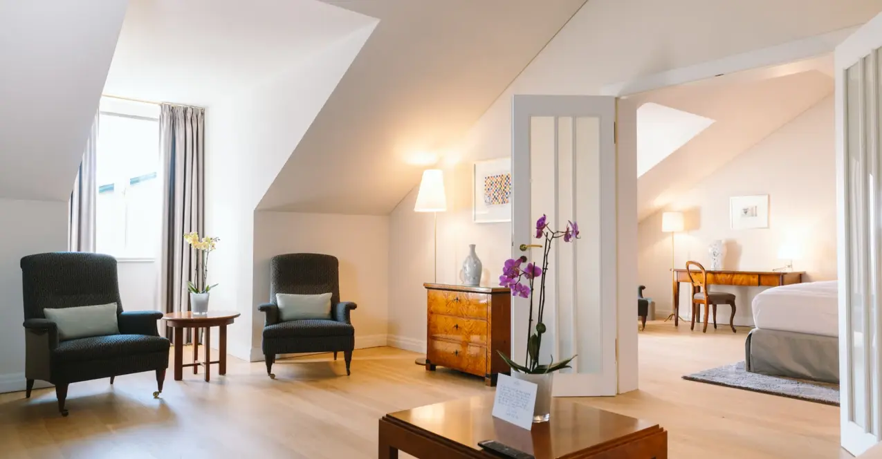 Hotelzimmer im Louis C. Jacob mit Holzboden, einem Tisch, Stühlen und einer Vase mit Blumen.