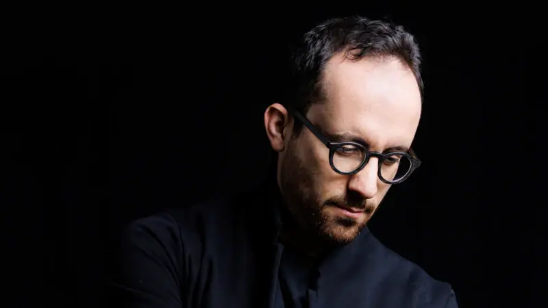 Ein Mann mit Brille in einem schwarzen Hemd.
