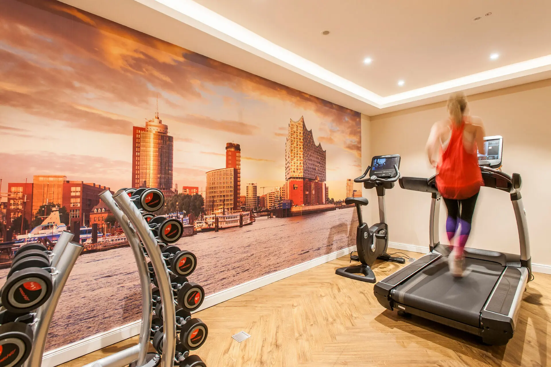 Eine Frau läuft auf einem Laufband im Fitness-Bereich des Louis C. Jacob in einem Raum mit einem großen Wandgemälde.