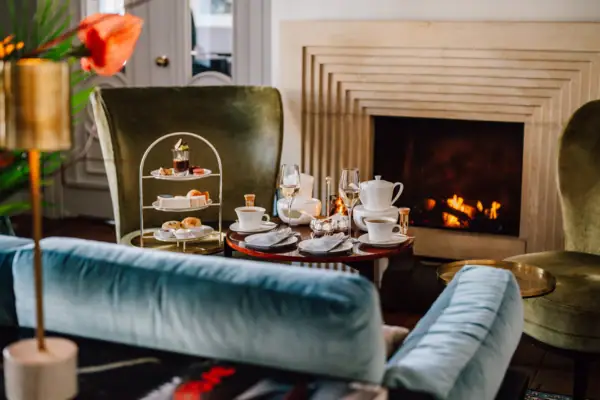 Vor dem Kamin in der Wohnhalle des Hotels Louis C. Jacob steht ein Sofa und ein Tisch mit einer englischen Teezeit. 