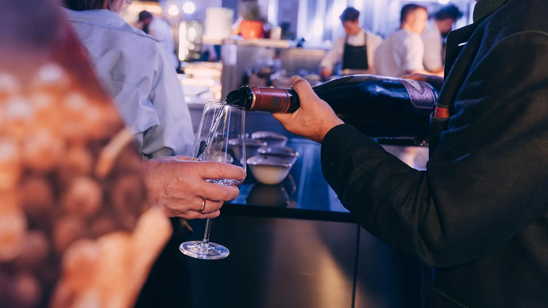Ein Mann schenkt Wein in ein Glas ein bei einer Küchenparty im Louis C. Jacob Hotel Hamburg.