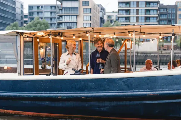 Zwei Männer und eine Frau stehen auf der Barkasse MS Jacob und unterhalten sich.