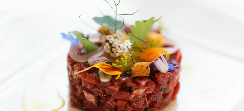 Steak Tartare mit Garnierung auf einem weißen Teller.