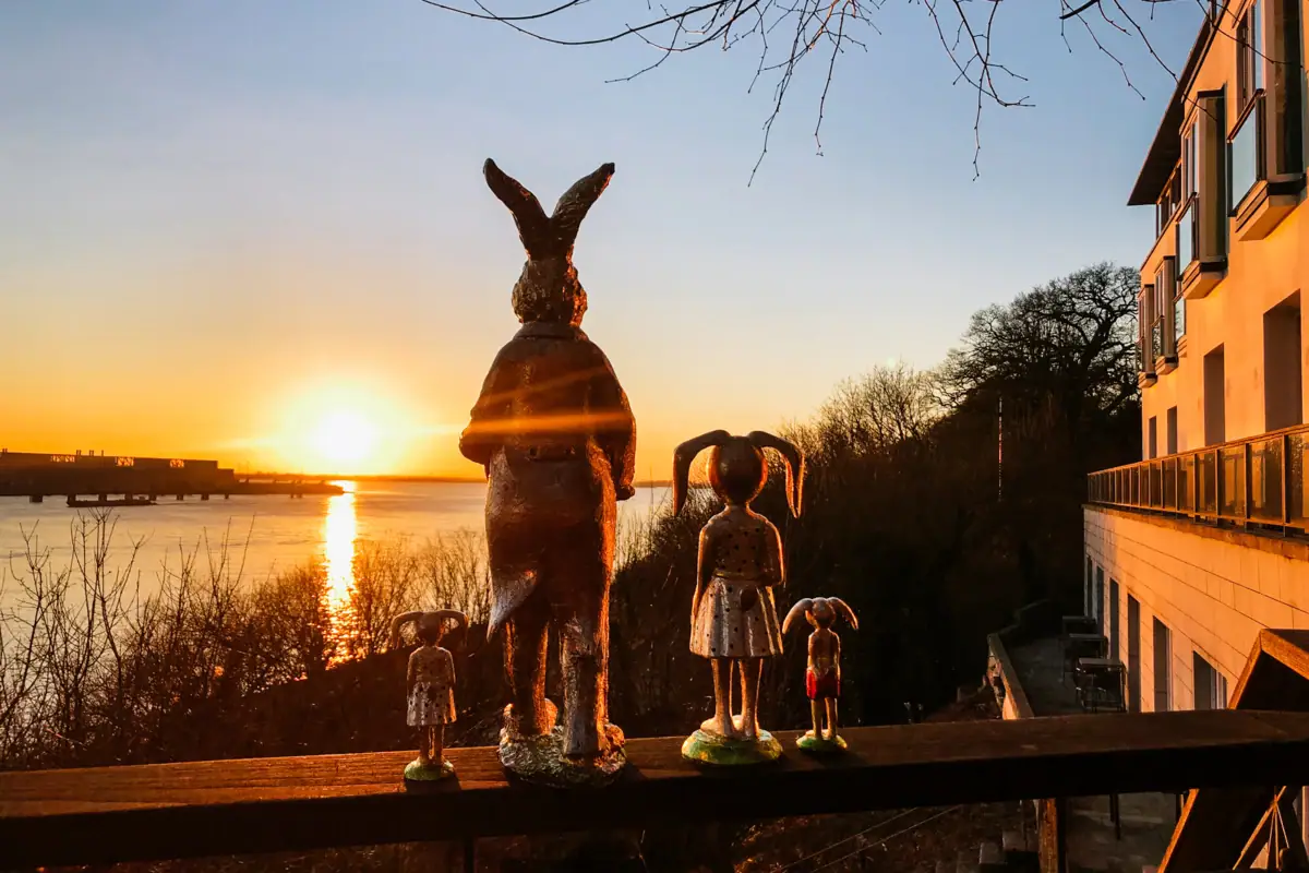 Osterhasenfiguren stehen auf der Reling der Lindenterrasse im Hotel Louis C. Jacob mit Blick auf die untergehende Sonne über der Elbe.