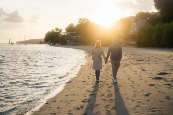 Ein Mann und eine Frau halten sich an den Händen am Strand.