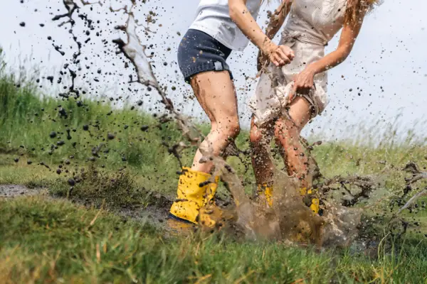 Pfütze und Gummistiefel Zwei Frauen springen mit gelben Gummistiefeln in eine Matschpfütze.