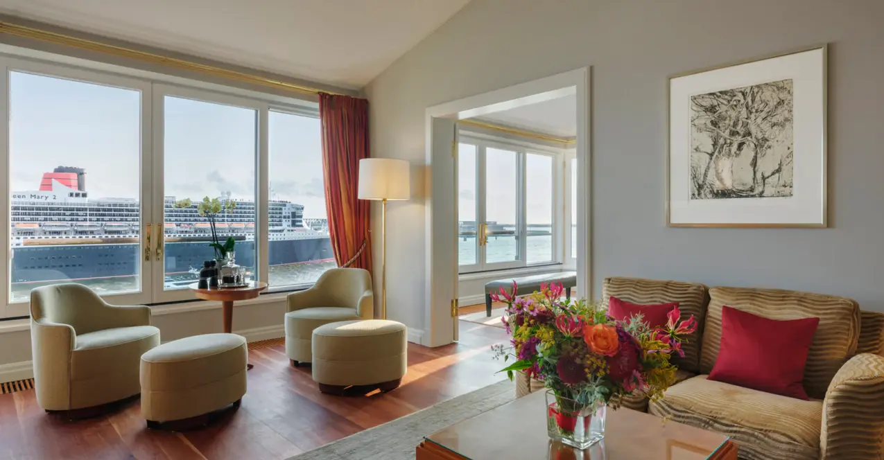 Wohnbereich der Elbsuite im Hotel Louis C. Jacob mit Couch, Sesseln und Couchtisch vor einem großem Fenster mit Blick auf die Elbe.