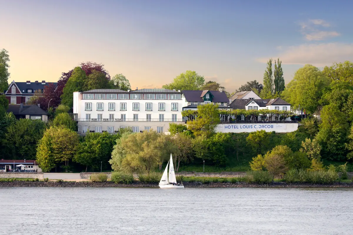 Das Hotel Louis C. Jacob von der Elbe aus betrachtet mit einem Segelboot in Front.
