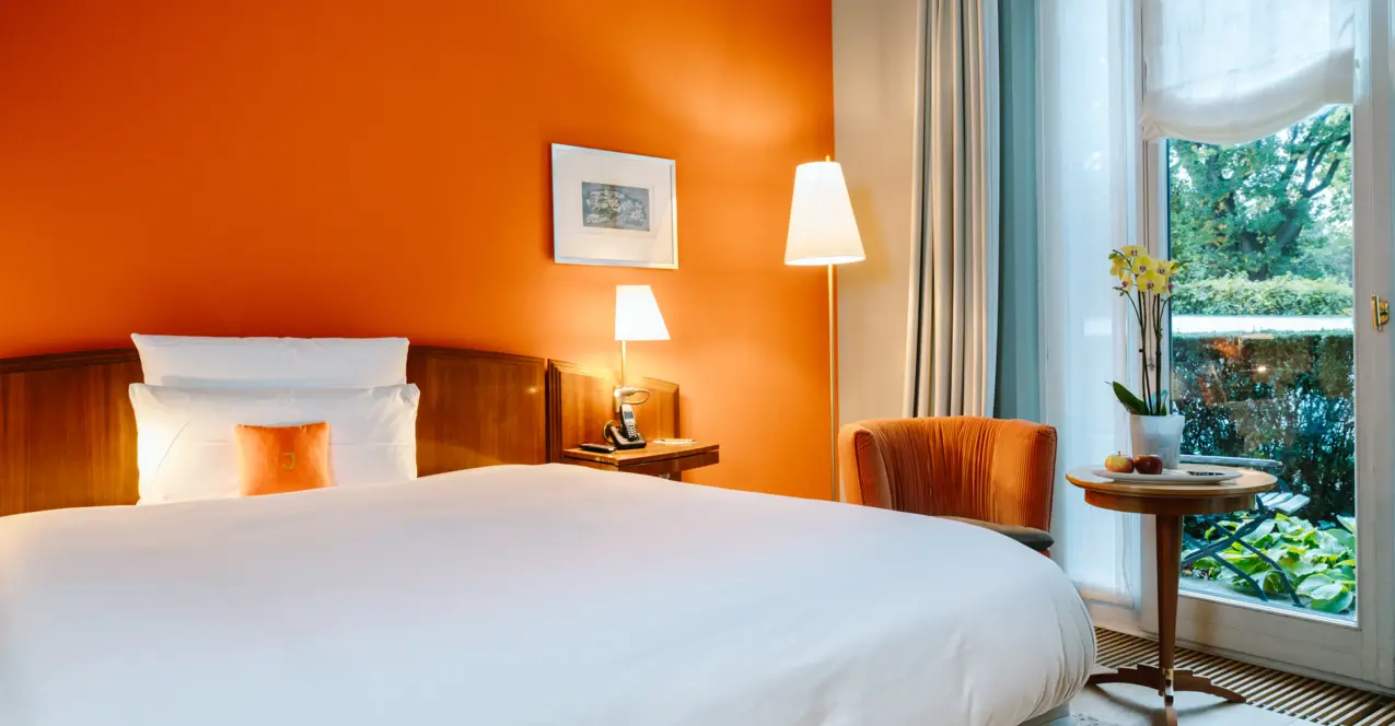 Ein Bett mit weißen Laken vor orangefarbenen Wänden.