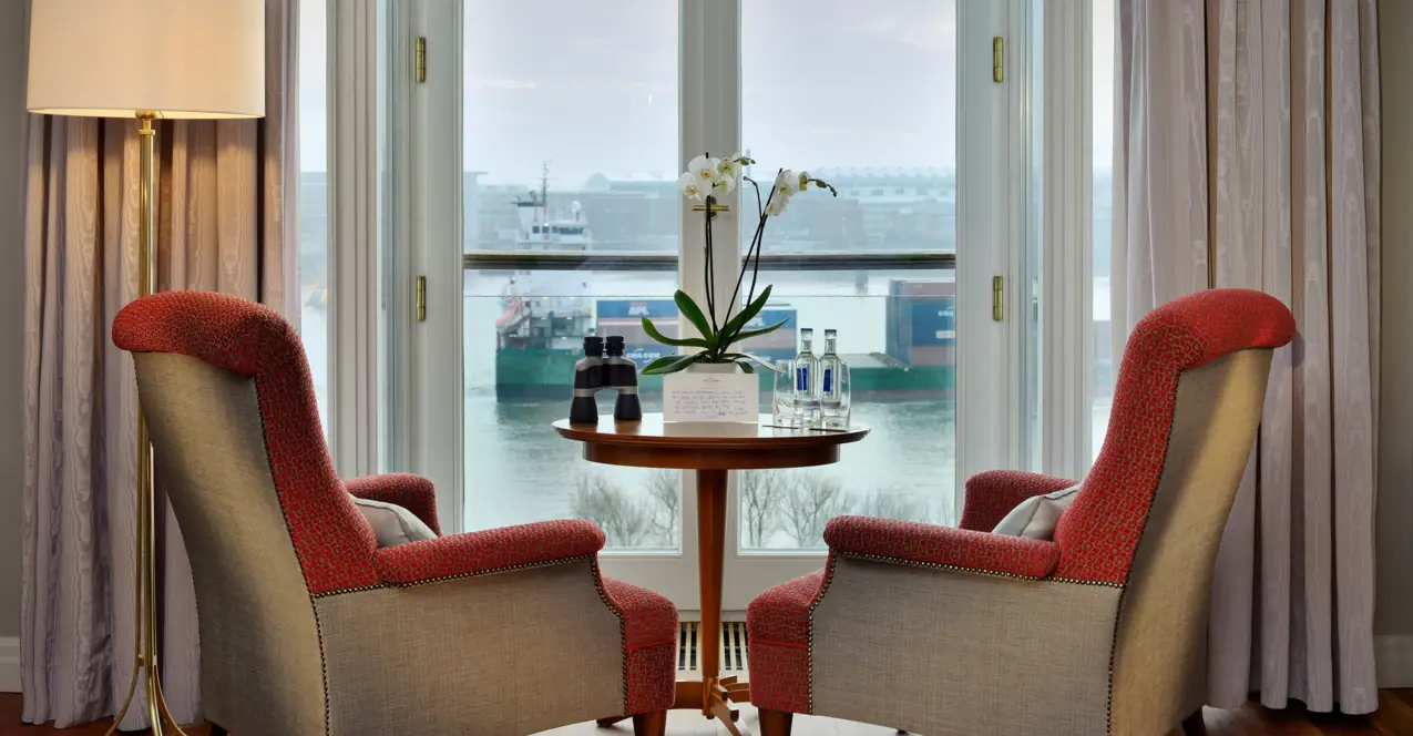 Hotelzimmer im Louis C. Jacob mit zwei Stühlen und einem Tisch vor einem Fenster mit Blick auf die Elbe.