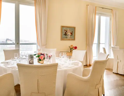 Eventlocation Ein Speiseraum mit einem gedeckten Tisch, Stühlen und einem Blumenarrangement.