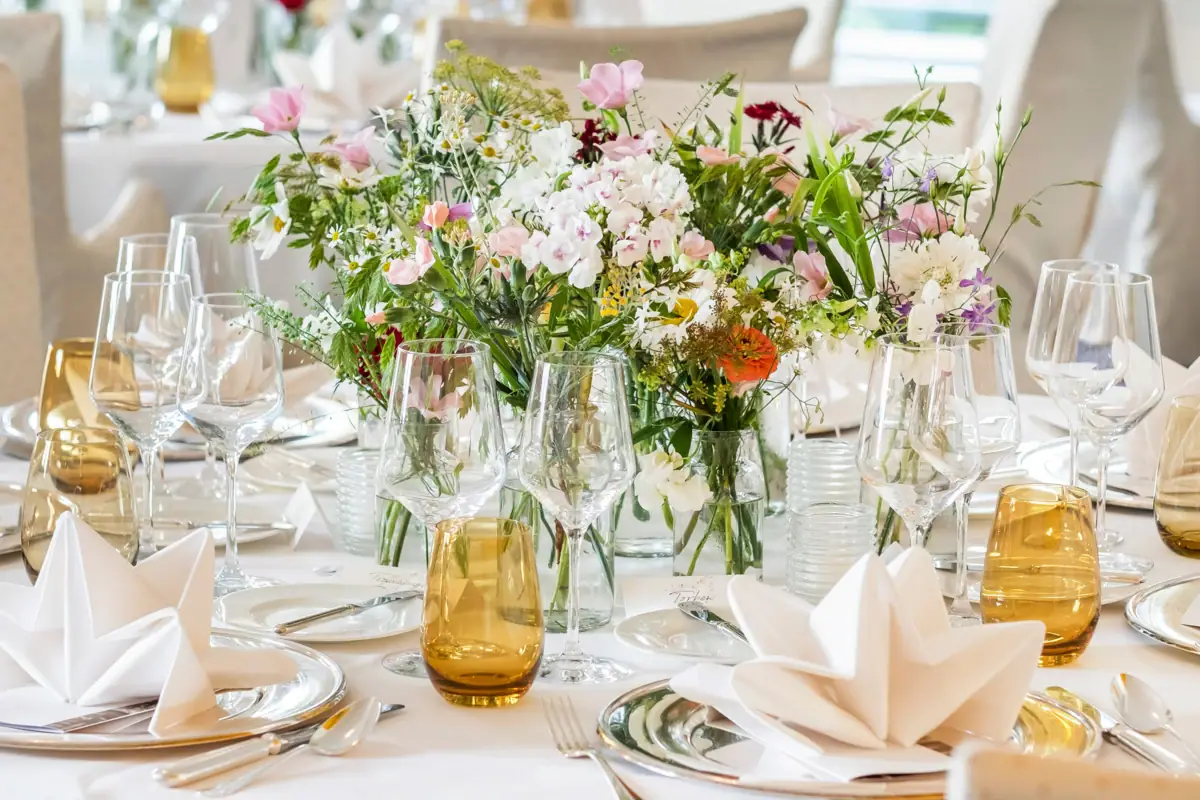 Ein festlich geschmückter Tisch mit Blumenarrangement und Weingläsern.