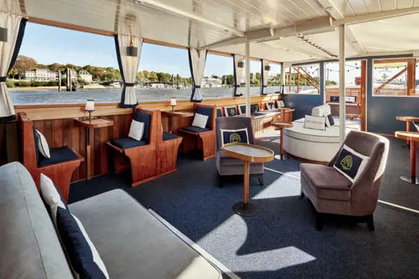 Der Innenraum der Barkasse MS Jacob mit Sitzbänken und Kissen und großen Fenstern, wodurch der Hamburger Hafen zu sehen ist.