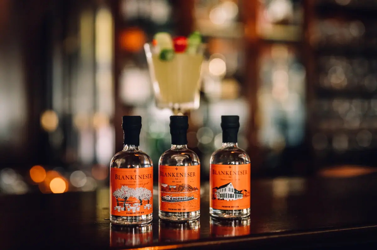 Drei Flaschen des Blankeneser Premium Dry Gin Collectors Edition "Hotel Louis C. Jacob" stehen auf einem hölzernen Bartresen.