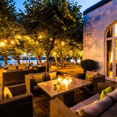 Beleuchteter Loungebereich der Lindenterrasse unter freiem Himmel mit Tischen und Sofas.