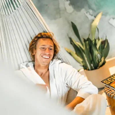Wellness im Urban Nature St. Peter-Ording Ein Mann im Bademantel liegt lächelnd in einer Hängematte.
