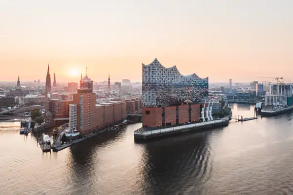 Stadtansicht von Hamburg mit der Elbe im Vordergrund und der Elbphillharmonie und der Stadt im Hintergrund bei Sonnenuntergang.