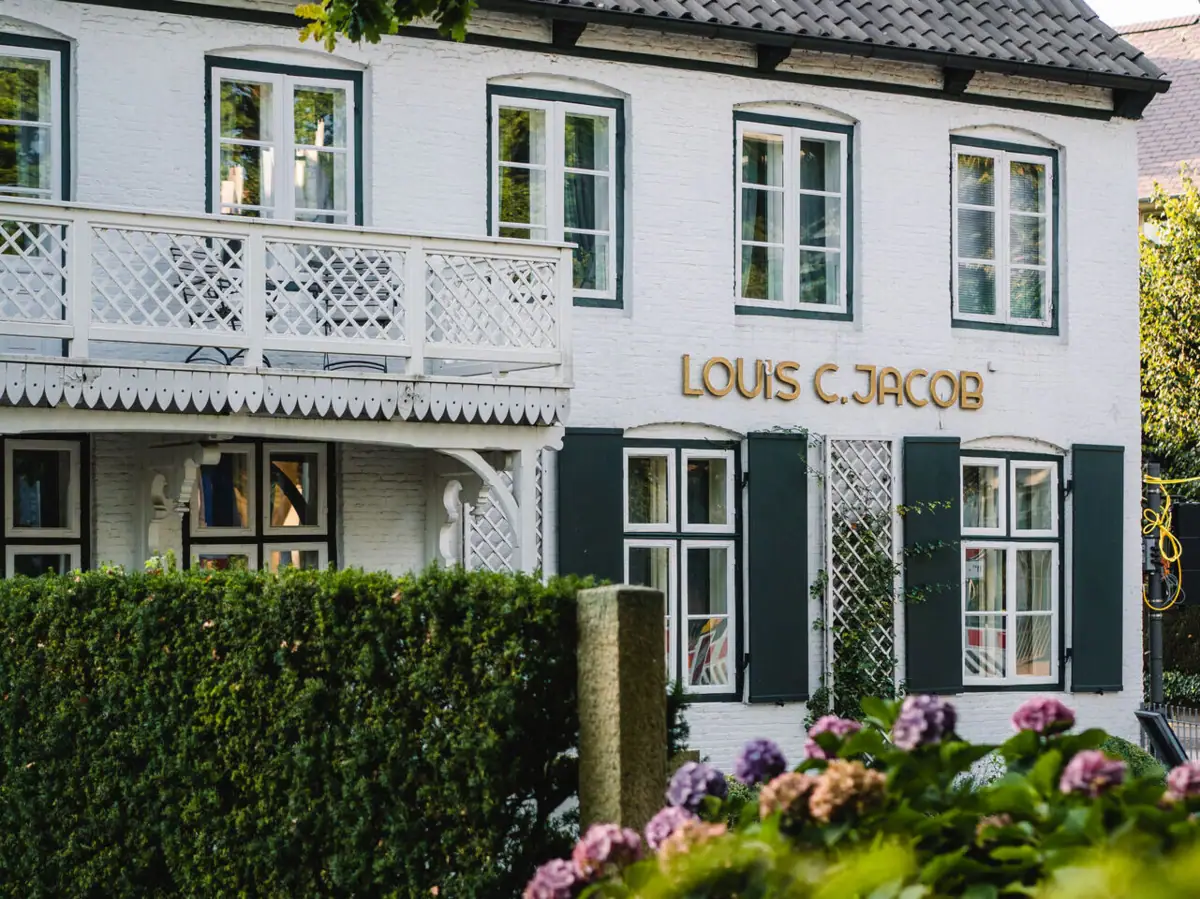 Louis C. Jacob Das Louis C. Jacob mit weißem Balkon und einer grünen Hecke davor.