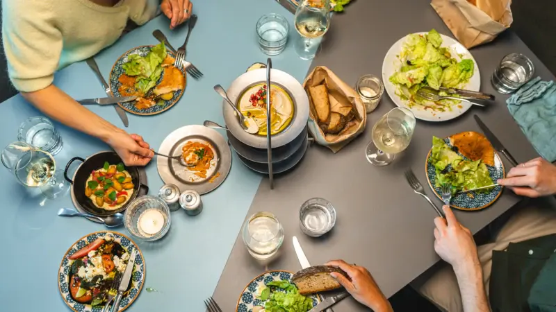 Food & Drinks im Urban Nature Hotel St. Peter-Ording Eine Gruppe von Menschen isst an einem Tisch, der mit vielen leckeren Speisen gedeckt ist.