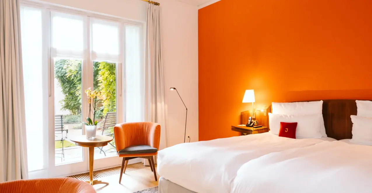 Ein Zimmer mit orangefarbenen Wänden und einem Bett, ausgestattet mit Kissen und Bettwäsche im Louis C. Jacob Hamburg.