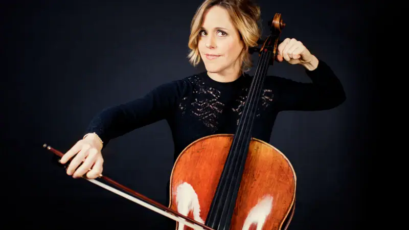 Sol Gabetta sitzt vor einem dunklen Hintergrund und spielt Cello.