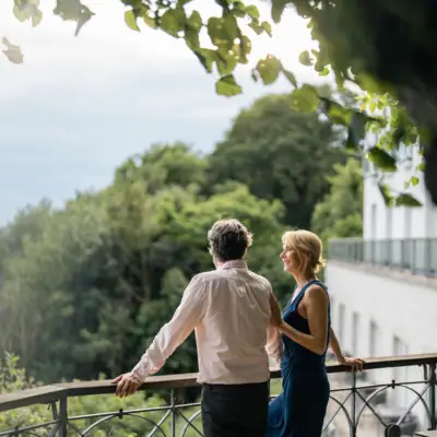 Ein Mann und eine Frau stehen nebeneinander an der Reling der Lindenterrasse des Hotels Louis C. Jacob und schauen auf die Elbe.