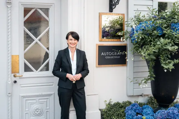 Direktorin vor dem Hoteleingang Eine Frau im Anzug steht vor einem Gebäude.