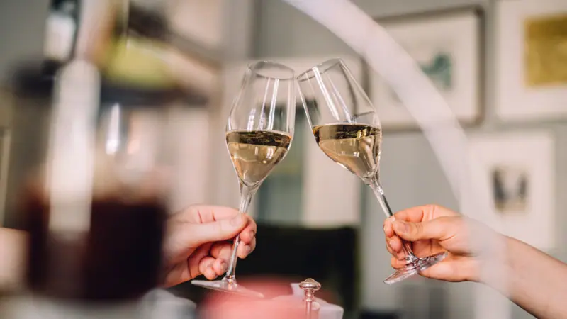 Zwei Hände stoßen mit Weingläsern an.