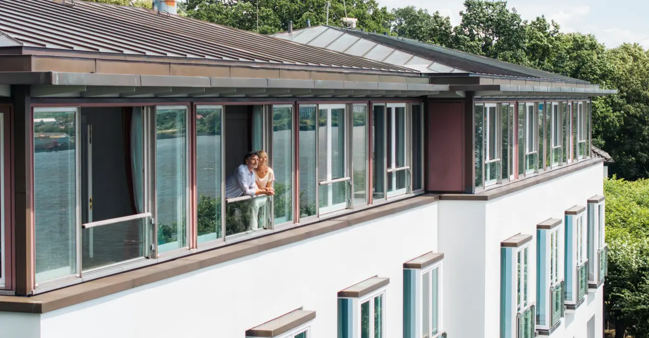 Weißes Gebäude mit Balkon und grüner Hecke.