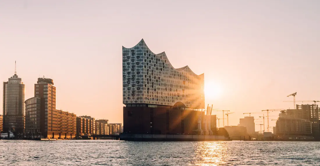 Blick auf einen See mit Stadtsilhouette und Booten im Hintergrund bei Sonnenuntergang.