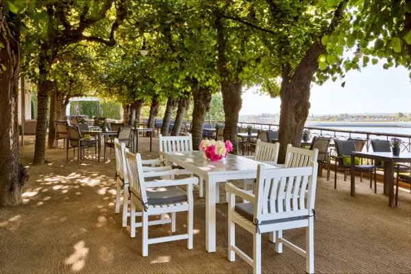 Die Lindenterrasse in Hamburg mit Tischen und Stühlen unter Bäumen mit Blick auf die Elbe.