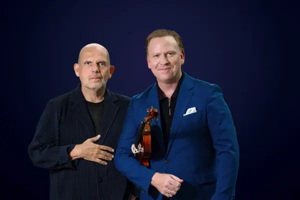 Zwei Männer posieren für ein Foto, beide lächelnd und in Blazer und Hemd gekleidet.