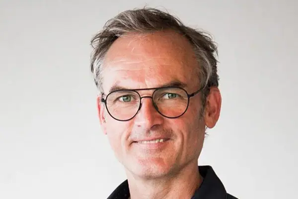 Ein Mann mit Brille und blauem Hemd lächelt.