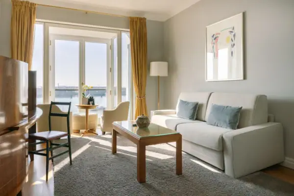 Ein gemütlicher Wohnbereich in einem Hotelzimmer mit Couch und Tisch sowie einem Balkon mit Blick auf die Elbe.