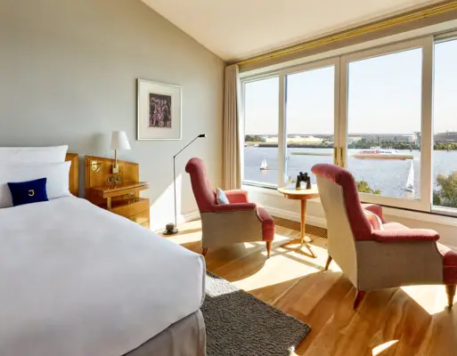 Zimmer mit Bett und Stühlen, Fenster mit Blick auf Wasser.