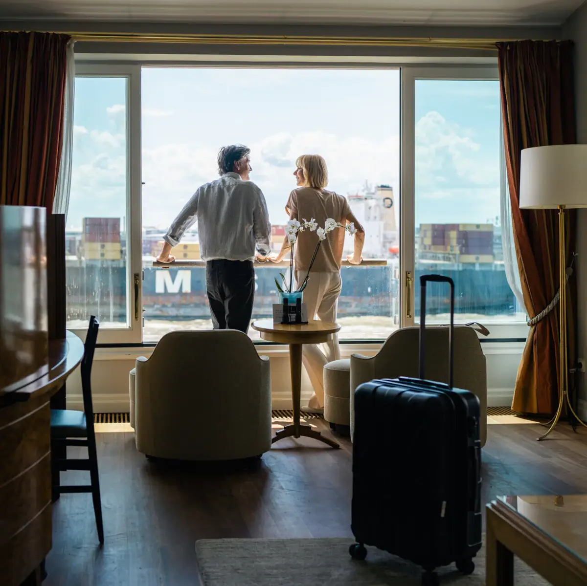Ein Mann und eine Frau stehen in einem mit Hotelzimmer an einem Fenster und schauen auf die Elbe.