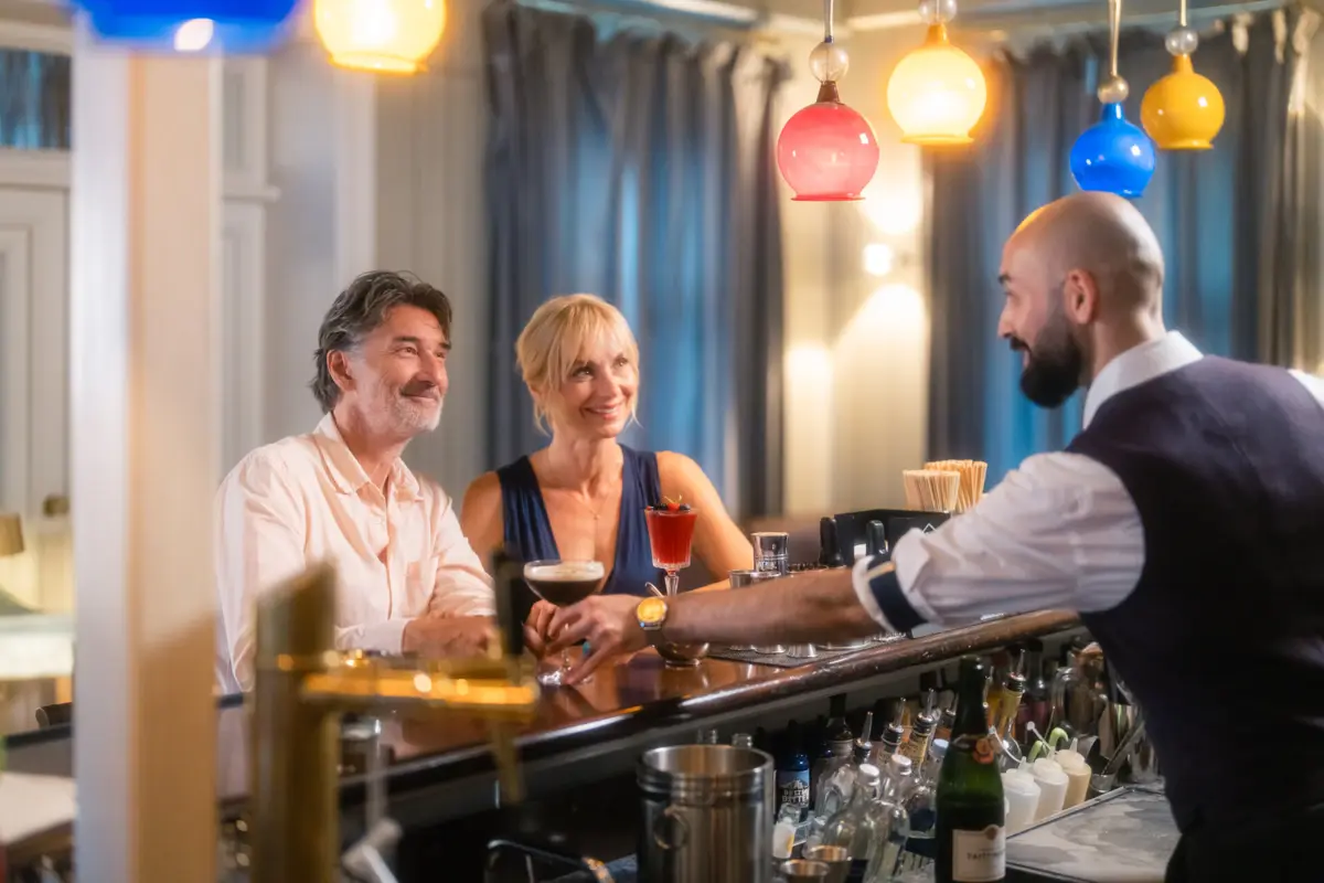 Zwei Menschen sitzen an der Jacobs Bar und der Barkeeper stellt ihnen Cocktails auf die Theke.