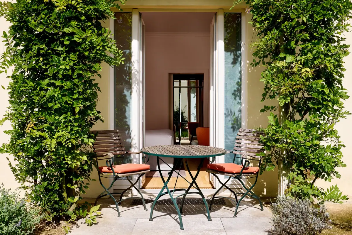 Blick auf eine Terrasse mit Tisch und Stühlen, begrünte Hauswand und Terrassentür