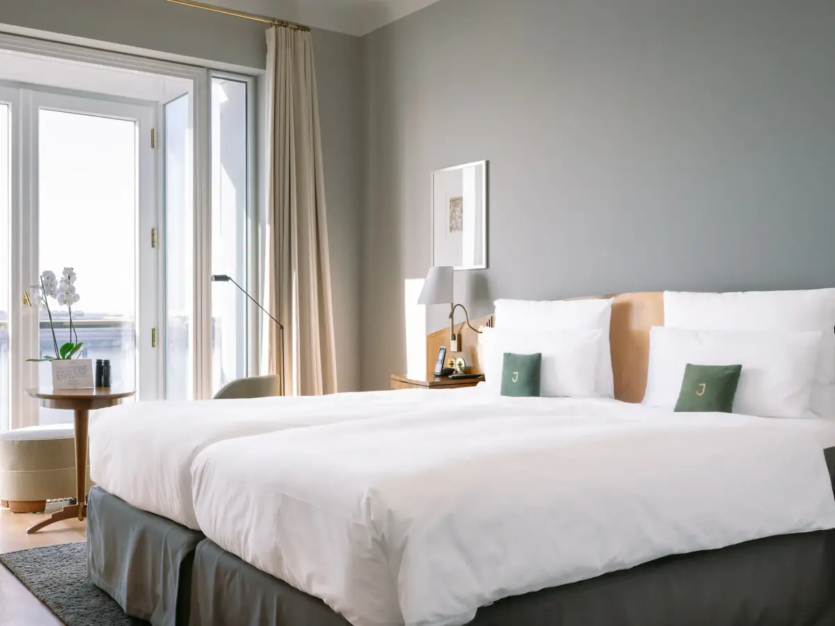 Ein Hotelzimmer mit einem Bett mit weißen Bettlaken und einem großen Fenster mit Blick auf die Elbe.