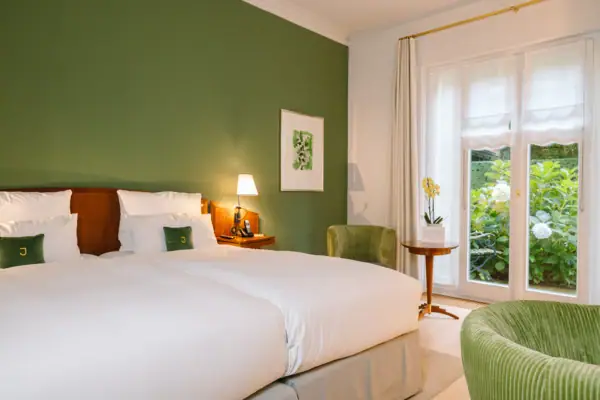 Hotelzimmer mit grünen Wänden, einem Bett und einer Terrasse ins Grüne im Hintergrund.